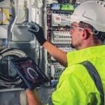 Protección dieléctrica contra riesgos eléctricos Trabajador con casco y guantes de seguridad, operando en un cuadro eléctrico, que representa la protección dieléctrica del calzado contra riesgos eléctricos.