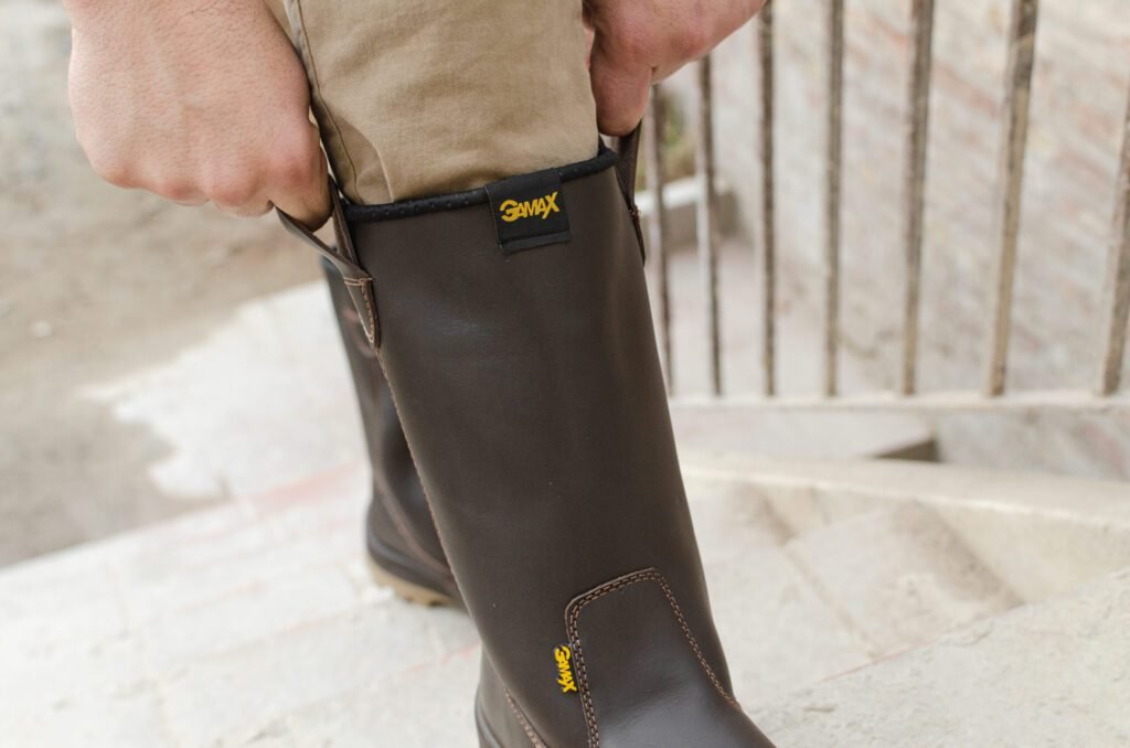 Una persona poniéndose una bota de seguridad robusta GamaX de color marrón, utilizando el tirador trasero para un calce rápido.