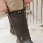 Bota Robusta 104A-114P Calce Fácil Una persona poniéndose una bota de seguridad robusta GamaX de color marrón, utilizando el tirador trasero para un calce rápido.